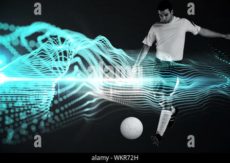 Joueur de football en blanc kicking against abstract blue fond noir brillant Banque D'Images