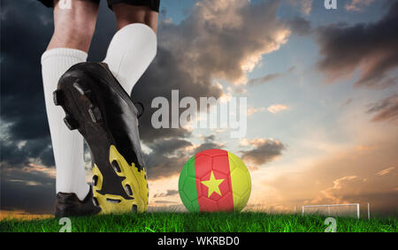 Image composite des coups de chaussure de football cameroun balle contre l'herbe verte sous le ciel bleu et orange Banque D'Images