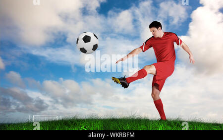 Joueur de football en rouge kicking against Green grass under blue sky Banque D'Images