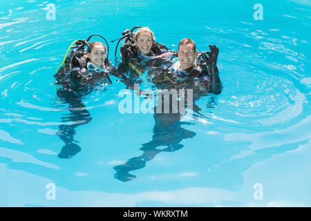 Smiling friends sur formation plongée en piscine lors d'une journée ensoleillée Banque D'Images