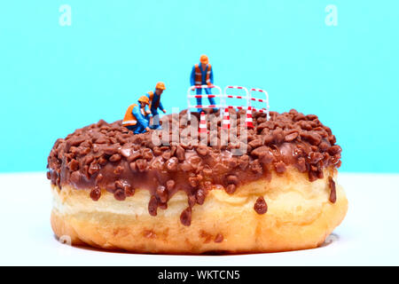 Image conceptuelle d'une figure miniature Ouvriers debout sur un beignet au chocolat en regardant le trou central Banque D'Images