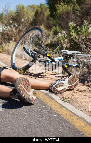 Cycliste couché sur la route après un accident lors d'une journée ensoleillée Banque D'Images