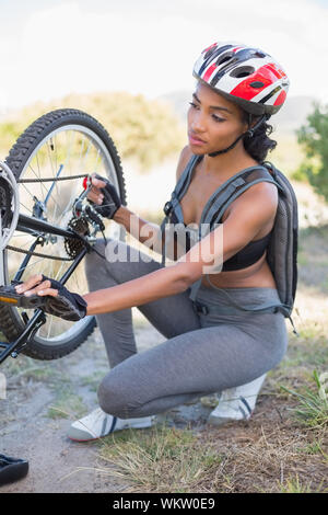 Fit woman fixant la chaîne sur son vélo sur une journée ensoleillée à la campagne Banque D'Images
