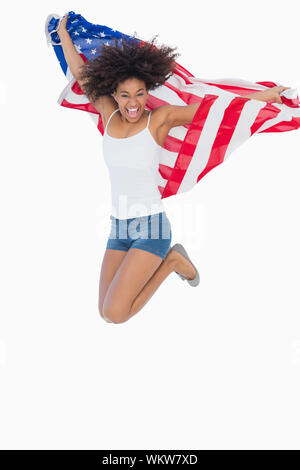 Jolie fille enveloppée de drapeau américain jumping and smiling at camera sur fond blanc Banque D'Images