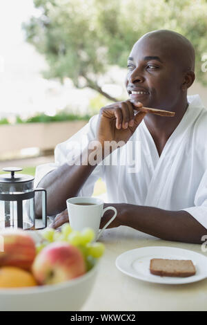 Bel homme en peignoir de prendre le petit déjeuner dehors sur une journée ensoleillée Banque D'Images