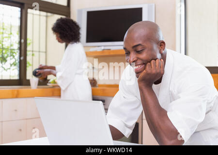 Bel homme en peignoir en utilisant laptop à la maison dans la cuisine Banque D'Images
