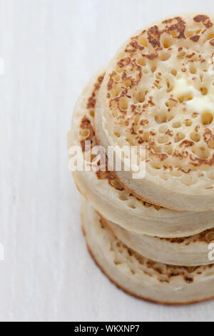 Tas de petites crumpets avec beurre fondu sur une planche en bois Banque D'Images