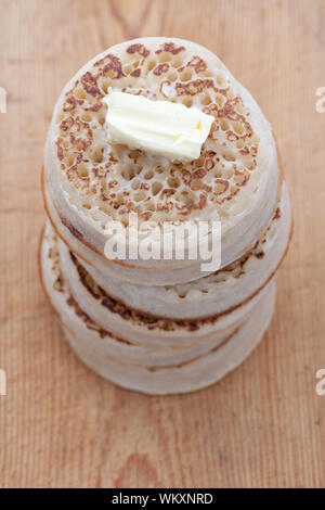 Tas de petites crumpets avec beurre fondu sur une planche en bois Banque D'Images