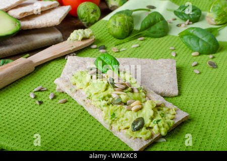 Accueil avocat propagation sur des biscottes avec graines de tournesol et de citrouille, de sésame et d'herbes épinards Banque D'Images