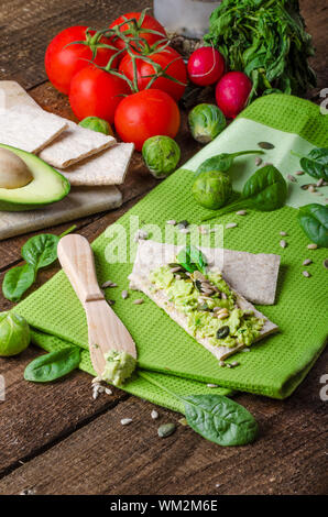 Accueil avocat propagation sur des biscottes avec graines de tournesol et de citrouille, de sésame et d'herbes épinards Banque D'Images