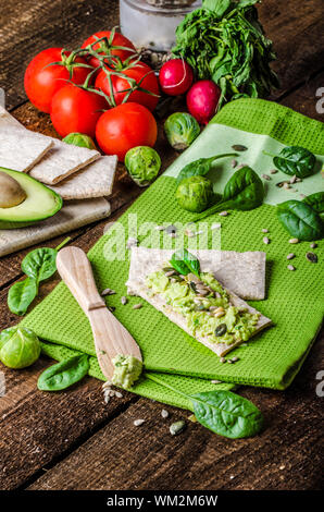 Accueil avocat propagation sur des biscottes avec graines de tournesol et de citrouille, de sésame et d'herbes épinards Banque D'Images