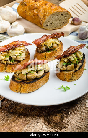 Petit-déjeuner rustique - ail rôties, poêlée de champignons, oeufs brouillés et bacon sur le dessus Banque D'Images