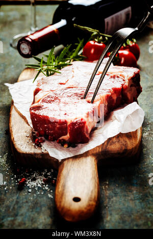 Marbré de steak de boeuf avec une bouteille de vin et des légumes sur fond sombre Banque D'Images