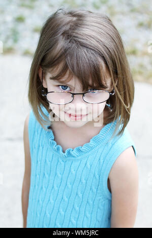 Petite fille à l'extérieur portant des lunettes et à la recherche jusqu'à la caméra. Banque D'Images