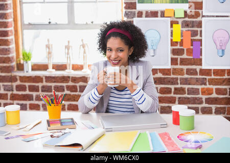 Portrait of smiling interior designer with coffee cup sitting at office desk Banque D'Images