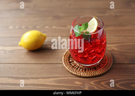 Verre de thé froid au citron boisson rouge isolé sur table en bois Banque D'Images