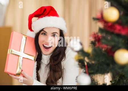 Surpris brunette holding un cadeau près de chez vous l'arbre de Noël Banque D'Images