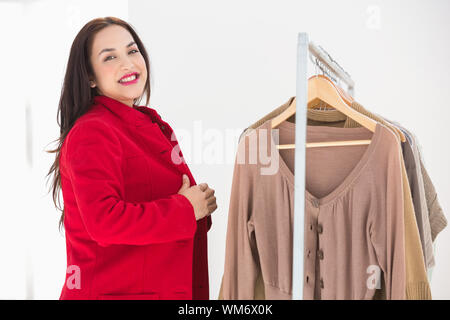 Smiling brunette d'essayer la veste rouge au magasin de vêtements Banque D'Images