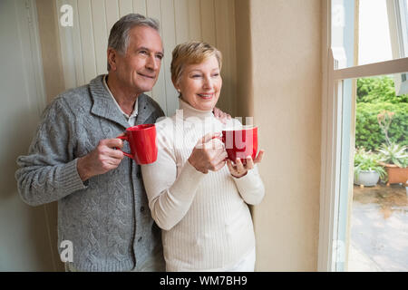 Senior couple holding mugs rouge à la maison dans la cuisine Banque D'Images
