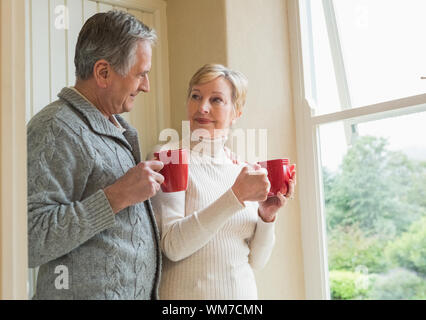 Senior couple holding mugs rouge à la maison dans la cuisine Banque D'Images