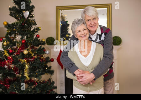 Senior couple hugging à côté de leur arbre de Noël à la maison dans le salon Banque D'Images