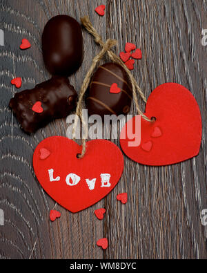 Deux coeurs rouges avec mot amour, chocolats et petits coeurs gros plan sur fond en bois foncé Banque D'Images