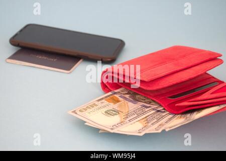 Portefeuille rouge avec des billets en dollars, un téléphone mobile et de passeport contre le fond bleu Banque D'Images