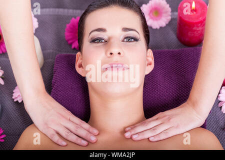 Close-up portrait de dessus d'une jeune femme brune attrayante ayant un massage facial relaxant, dans un centre spa de fantaisie, avec des bougies parfumées un Banque D'Images