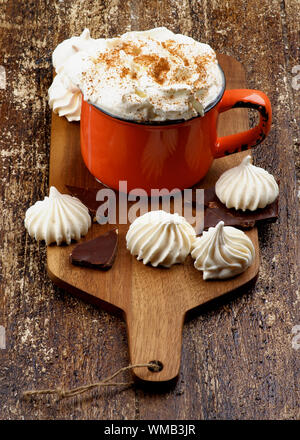Les meringues et tasse de chocolat chaud avec de la crème fouettée et la cannelle sur une planche à découper sur fond de bois rustique Banque D'Images