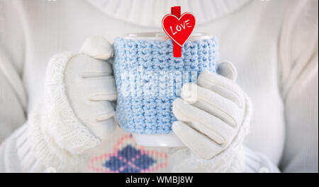 La laine tricotée tasse de mains humaines. Avec coeurs rouges et le mot amour. Valentines Day. Banque D'Images