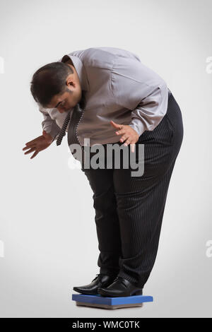 L'homme obèse en vêtements officiels debout sur une machine de pesage choqué de voir son poids Banque D'Images