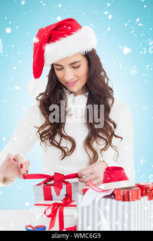 Happy brunette in santa hat cadeaux emballage contre fond bleu avec vignette Banque D'Images
