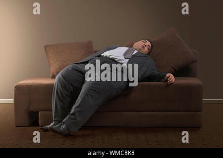 Homme d'obèses dans les vêtements officiels de dormir sur un canapé à la maison Banque D'Images