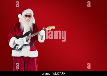 Le Père Noël joue de la guitare avec des lunettes contre fond rouge Banque D'Images