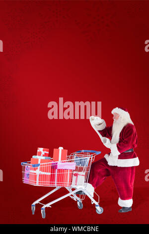 Santa pousse un panier lors de la lecture à l'arrière-plan rouge Banque D'Images