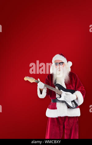 Le Père Noël joue de la guitare avec des lunettes contre fond rouge Banque D'Images