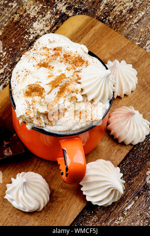 Tasse de chocolat chaud avec de la crème fouettée, de la cannelle et des meringues sur une planche à découper sur fond de bois rustique. Vue d'en haut Banque D'Images