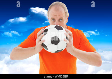 Fan de football nerveux holding ball contre ciel bleu avec des nuages Banque D'Images