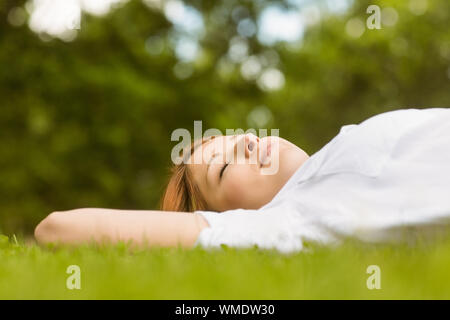 Jolie rousse couché avec les yeux fermés sur l'herbe dans le parc Banque D'Images