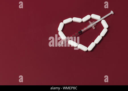 Pilules blanches en forme de coeur avec une seringue d'un liquide rouge sur fond rouge. Mise à plat de style. Copier l'espace. Médecine, Pharmacie et soins de concep Banque D'Images