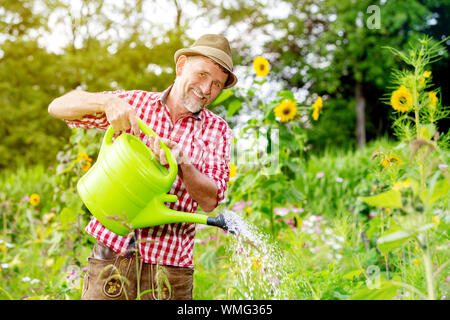 Portrait of handsome man standing bavarois dans le jardin et arrosage des fleurs Banque D'Images