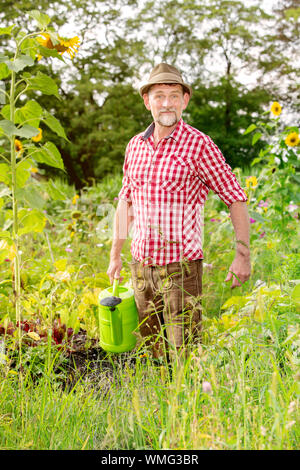 Portrait of handsome man standing bavarois dans le jardin et arrosage des fleurs Banque D'Images