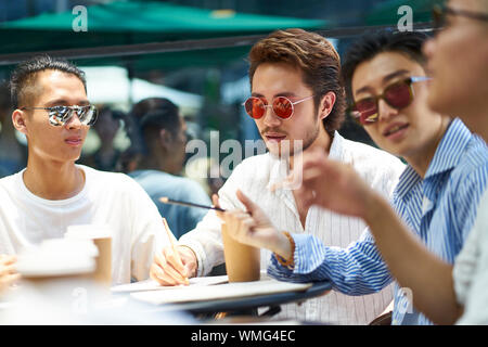 Les jeunes étudiants asiatiques ayant un groupe de discussion à un café-restaurant en plein air Banque D'Images