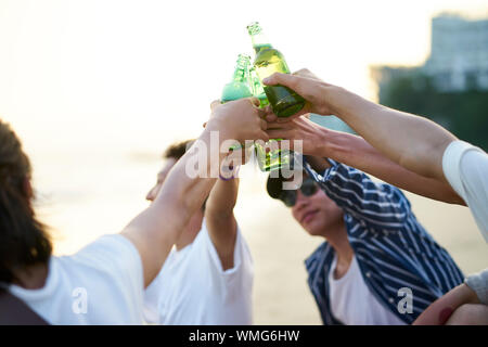 Groupe de jeunes adultes asiatiques Men sitting on beach with Bottles of Beer Banque D'Images