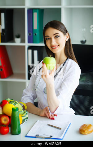 La santé. L'alimentation saine. La nutritionniste tient dans les mains de frais vert pomme. Les fruits et légumes frais sur la table. Heureux Médecin. Haut Banque D'Images