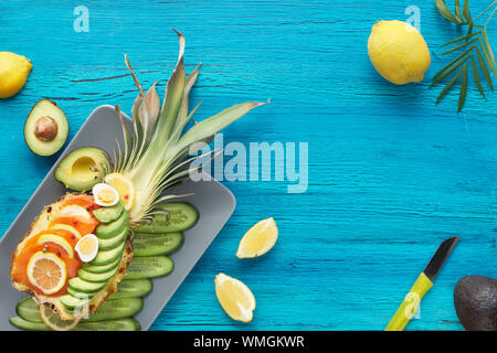 Vue de dessus sur ananas bateaux avec du saumon fumé et des tranches d'avocat au citron et oeufs de caille, télévision jeter sur fond texturé turquoise Banque D'Images