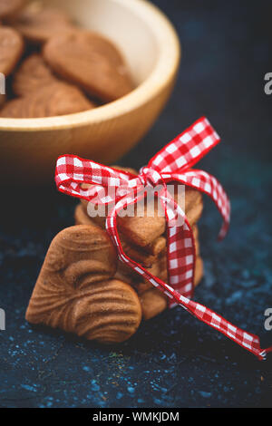 Pile de Ginger cookies en forme de coeur pour la Saint-Valentin avec ruban rouge-blanc sur fond bleu foncé Banque D'Images