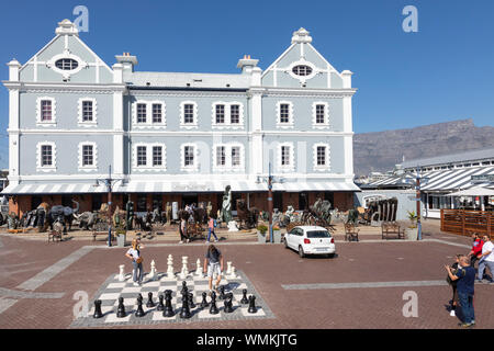 Les touristes admirant le conseil d'échecs en plein air en face du port de commerce avec son affichage de la sculpture africaine, V&A Waterfront, Cape Town, Sout Banque D'Images