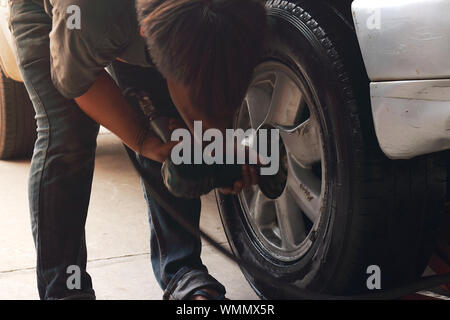 Un mécanicien utilise une clé à chocs pour serrer les écrous de roue sur le moyeu d'une voiture grise. Banque D'Images