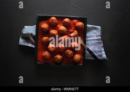 Des boulettes en sauce tomate rouge sur un plateau noir et un noir d'examen. Voir ci-dessus de la viande savoureux plat suédois. Mise à plat de table pour un dîner. Banque D'Images